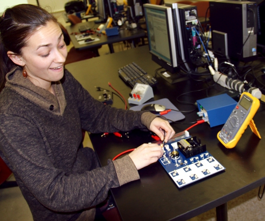 Rachel testing bulbs in the circuit board with an exaggerated smile on her face.