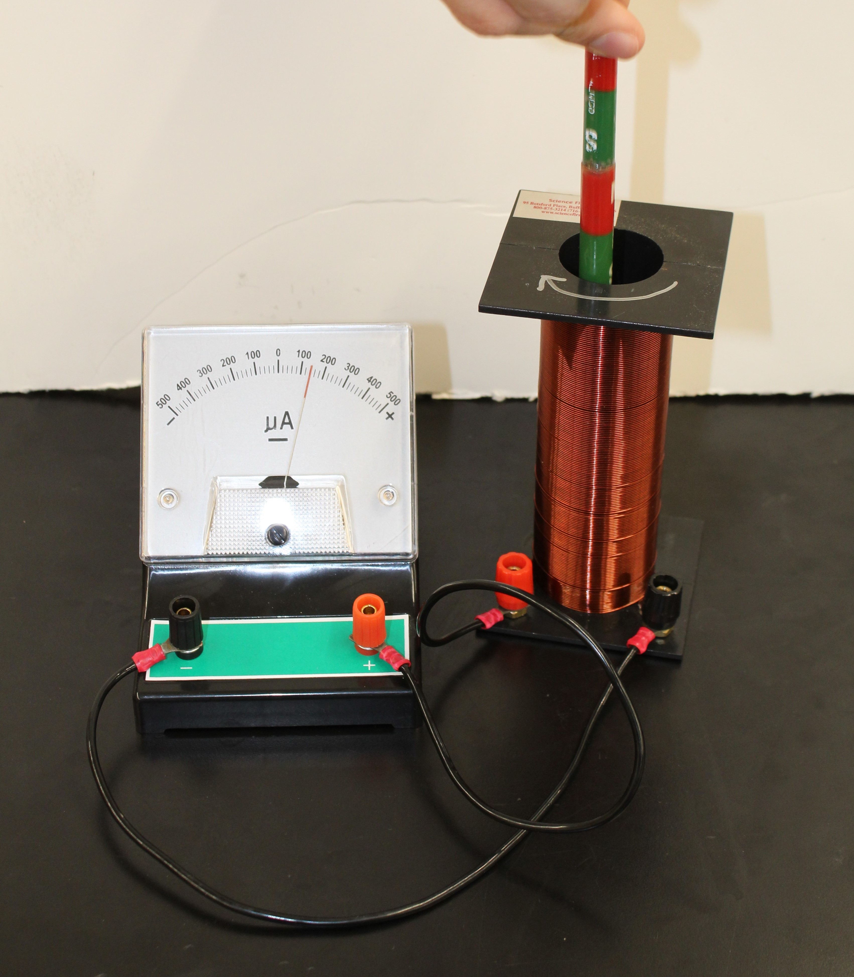 The Galvanometer hooked up to the solinoid with two spade wires. A Hand is lowering two barmagnets stuck end on end into the solenoid and the needle on the Galvanometer is deflected to the right to about 150 microamps
